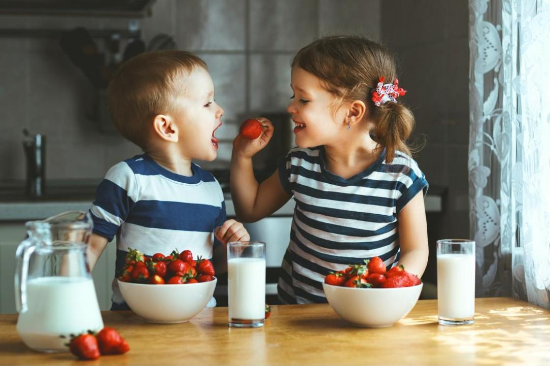 Two young children eating strawberries and drinking milk