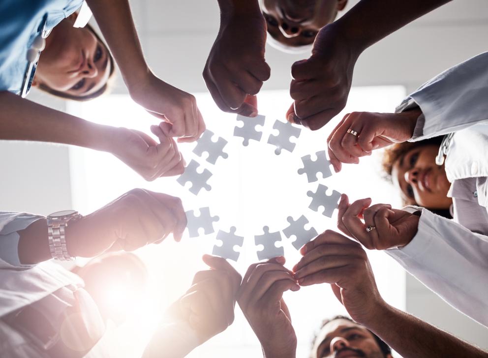 Low angle shot of a group of doctors forming a huddle while each holds a puzzle piece inside of a hospital